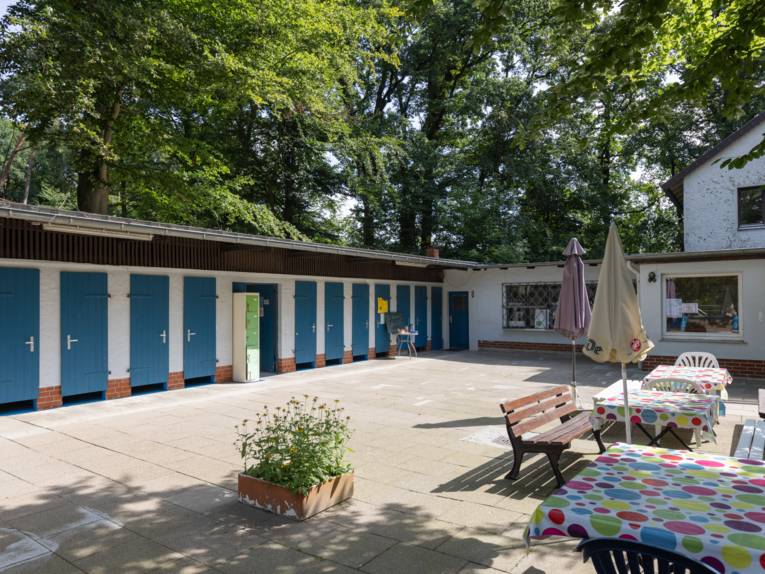 Gebäude mit blauen Holztüren, davor eine Terrasse mit Tischen und Bänken/Stühlen