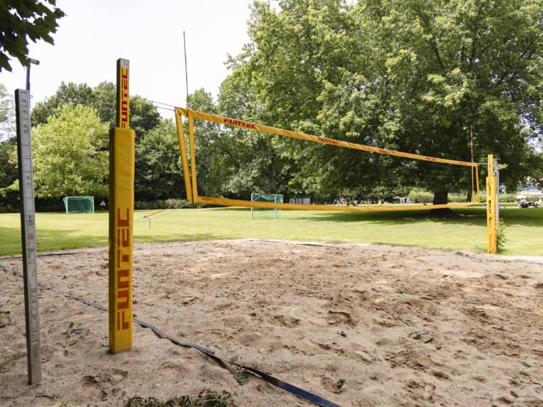 Beachvolleyballfeld mit gespanntem Netz, im Hintergrund Fussballtore