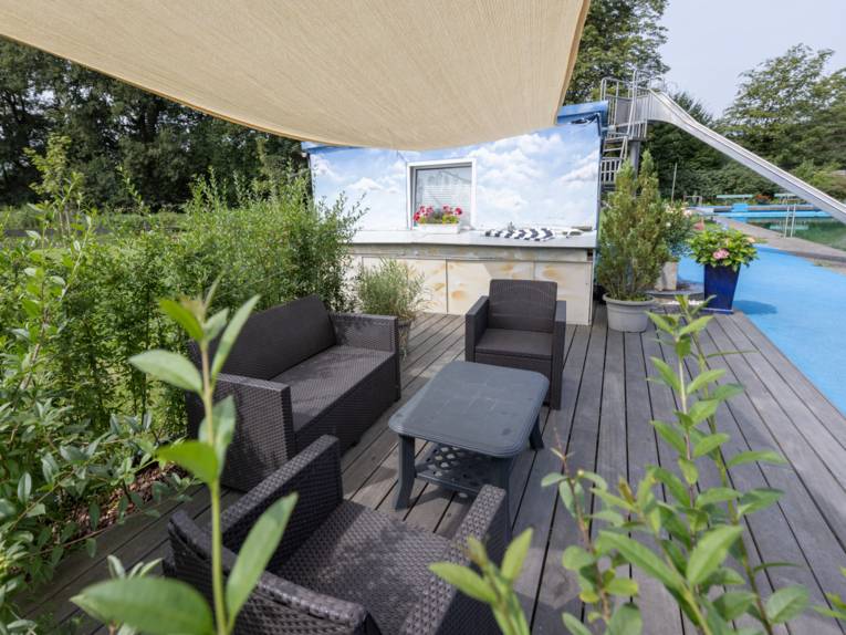 Sitzecke mit Tisch neben dem Schwimmbeckenrand unter einem Sonnensegel