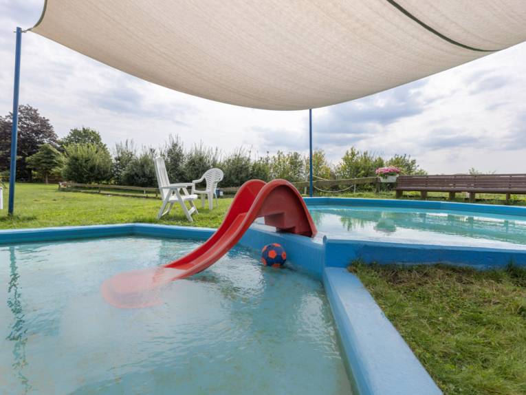 Rutsche zwischen zwei ineinander übergehenden flachen Becken mit einem Sonnensegel und kleiner Rutsche