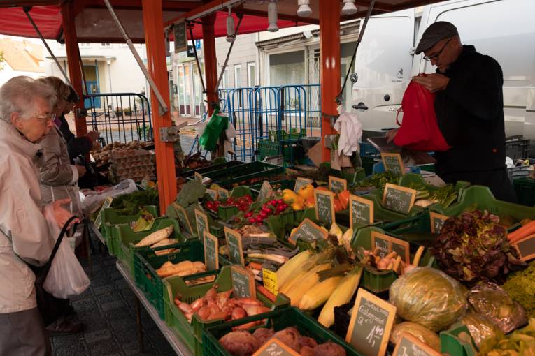Kund*innen kaufen an einem Obst- und Gemüsestand Waren ein.
