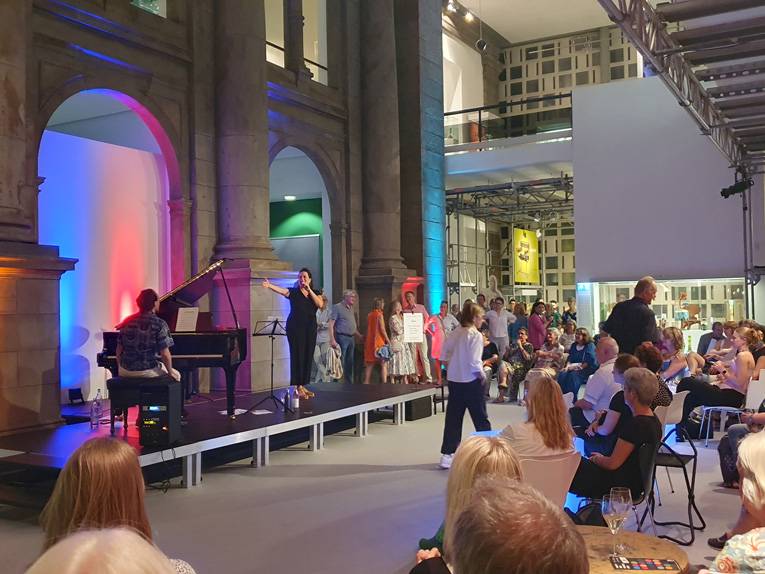 Eine Sängerin und ein Pianist stehen vor Publikum auf einer Bühne im Museum August Kestner