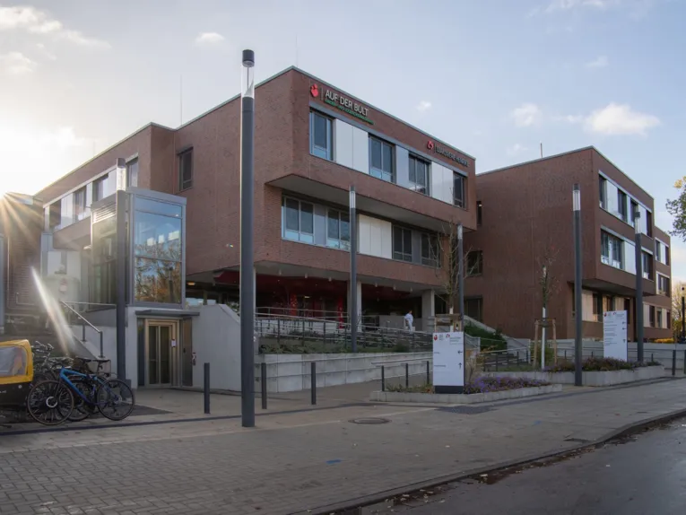 Außenansicht des Kinder- und Jugendkrankenhauses AUF DER BULT in Hannover mit roter Backsteinfassade, großen Fensterfronten, barrierefreiem Eingangsbereich und Fahrrädern im Vordergrund bei Sonnenschein.
