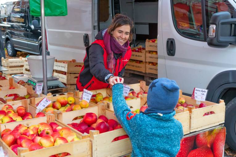 Eine Verk&auml;uferin reicht einem Kind einen Apfel.