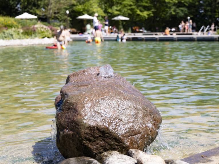 Flacher Badebereich mit einem gro&szlig;en Stein, aus dem Wasser l&auml;uft im Vordergrund