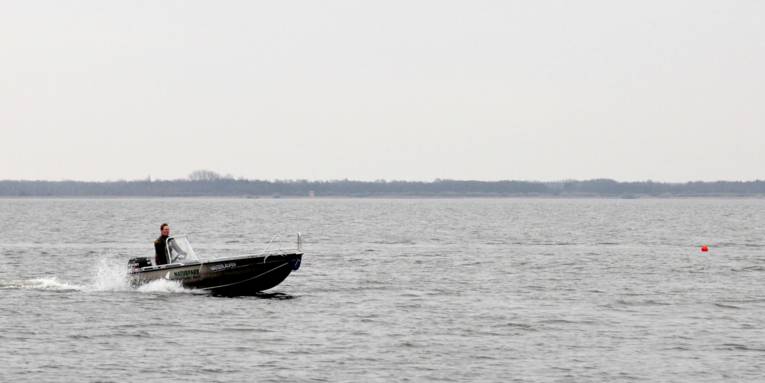 Ein Naturparkranger fährt mit dem Boot "Wasserläufer" über das Steinhuder Meer, an einer roten Boje entlang.