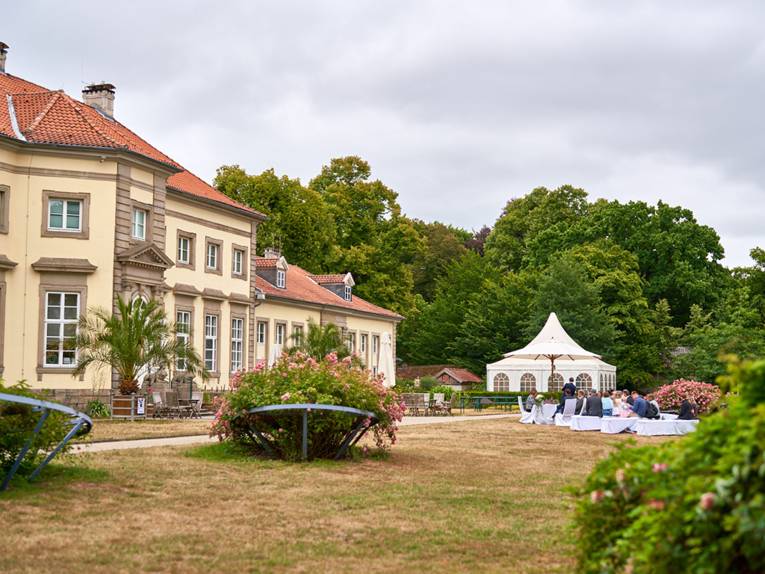 Ein mit Blumen und Kerzen geschmückter Tisch und drei Stühle mit weißen Stuhlhussen im Grünen.