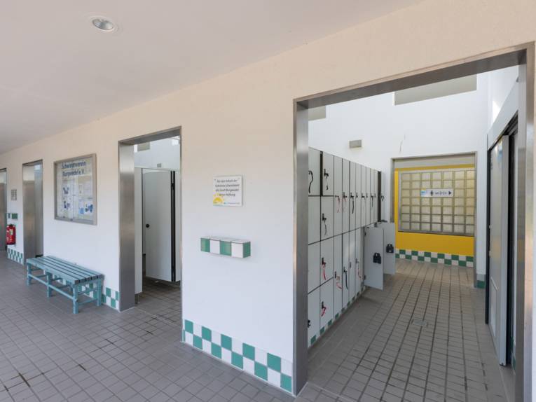 Gekachelter Flur von dem aus es in verschiedene Räume geht, in denen Umkleiden und Schliessfächer zu sehen sind