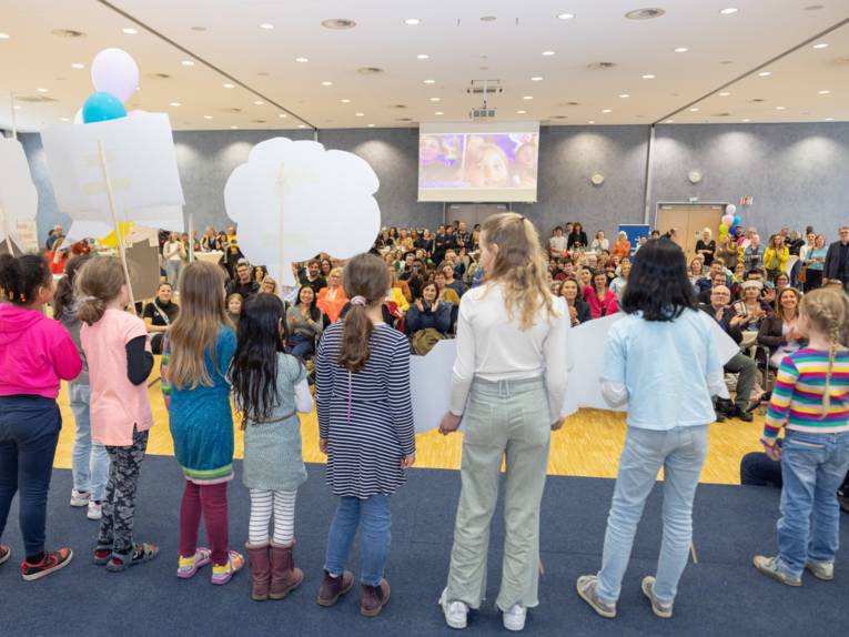 Grundschulkinder auf einer Bühne, von hinten fotografiert.