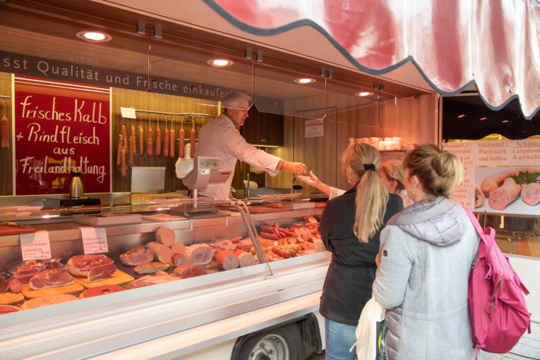 Ein Fleischerei-Verkäufer verkauft Waren an seine Kundschaft auf dem Wochenmarkt.