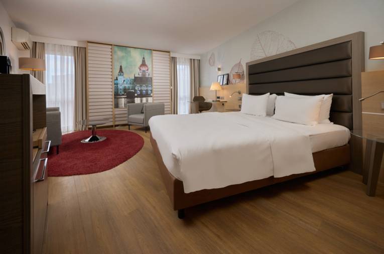 Modernes Hotelzimmer mit Doppelbett, Schreibtisch, Sitzecke und Wandbild des Neuen Rathauses Hannover.