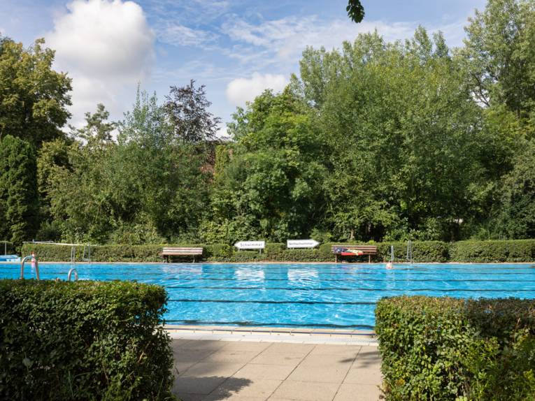 Schwimmbecken von Hecken umschlossen, im Vordergrund ein Durchgang zur/von der Liegewiese