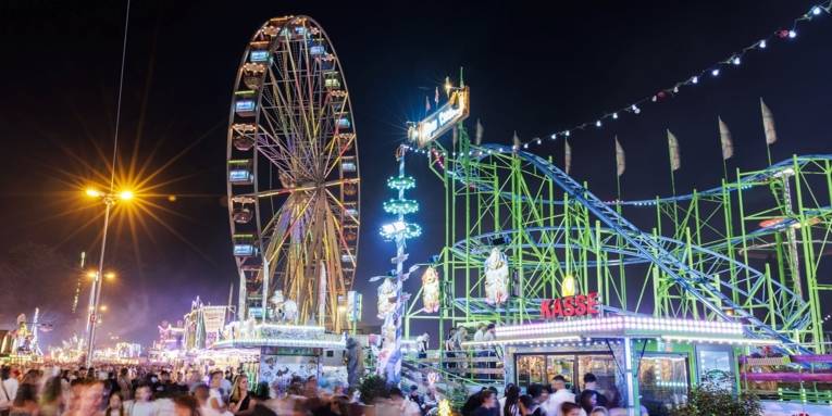 Es handelt sich um ein Bild vom Schützenfest Hannover. Auf dem Bild befindet sich ein Riesenrad und ein weiteres Karussell, sowieEssensstände und Menschenmengen.