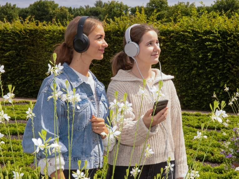 Zwei Personen mit Kopfhörern in einem Garten.