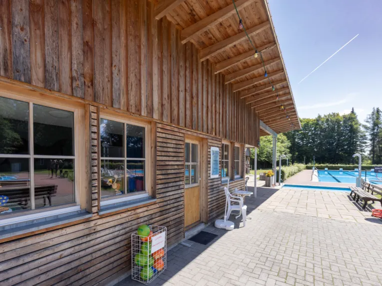 Freibad: Holzverkleidetes Geb&auml;ude, im Hintergrund Schwimmbecken