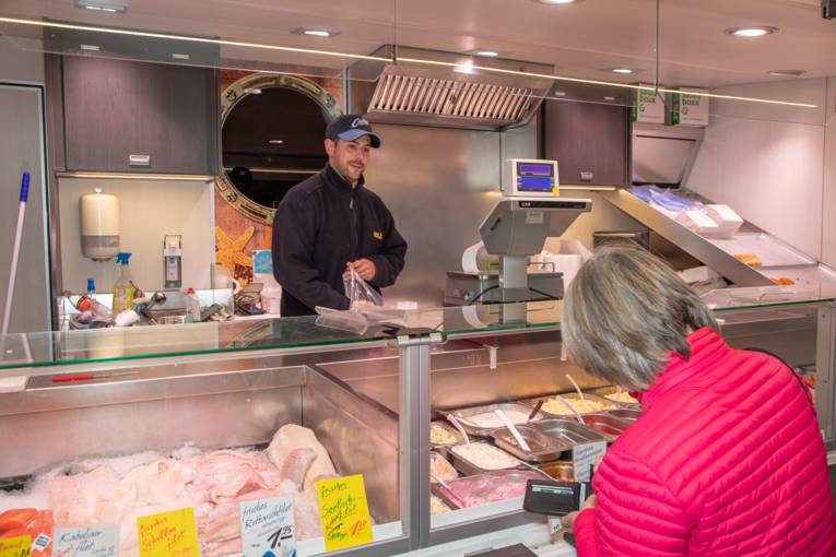 Frische Fischfilets in einem Marktwagen; eine Kundin kauft Waren.