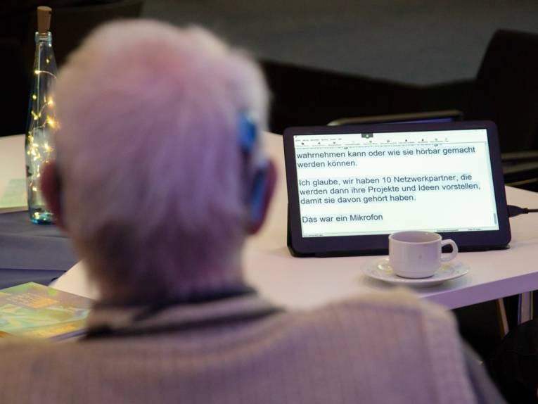 Ein Herr mit Cochlear-Implantat liest den Text auf einem Tablett vor ihm