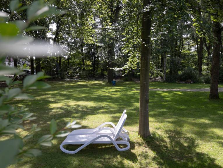 Zwei Liegestühle unter Laubbäumen auf einer Wiese stehend