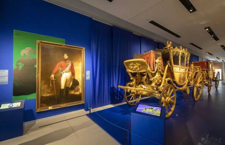 Das Bild zeigt eine prächtige historische Kutsche und ein Gemälde im Museum Schloss Herrenhausen, Hannover, im Rahmen einer Museumsführung.