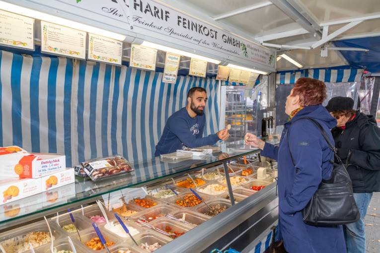Ein Feinkosth&auml;ndler bietet einer Kundin Waren zum probieren an.