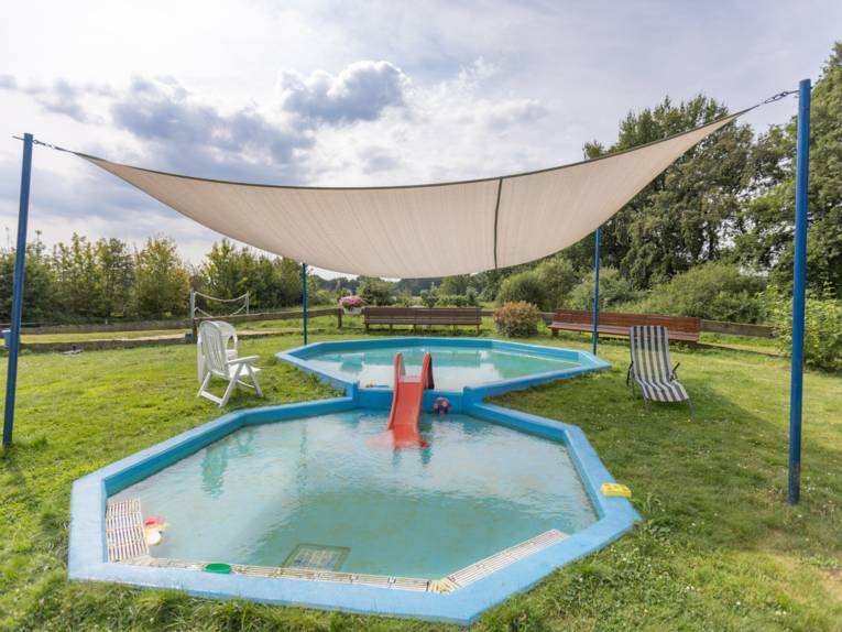 Zwei ineinander übergehende flache Becken mit einem Sonnensegel und kleiner Rutsche