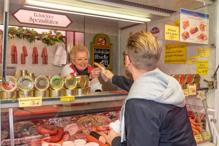 En butiksassistent rækker en kunde en pølse.