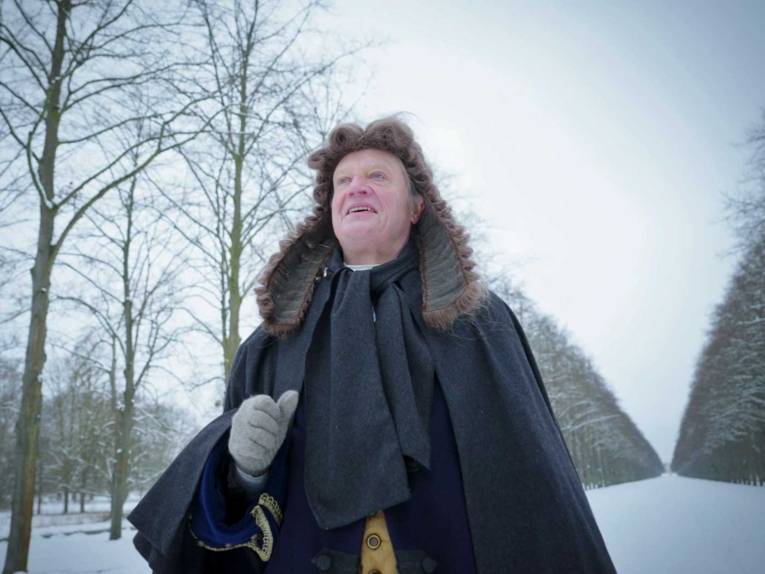 Mann mit historischer Perücke in verschneiter Allee.