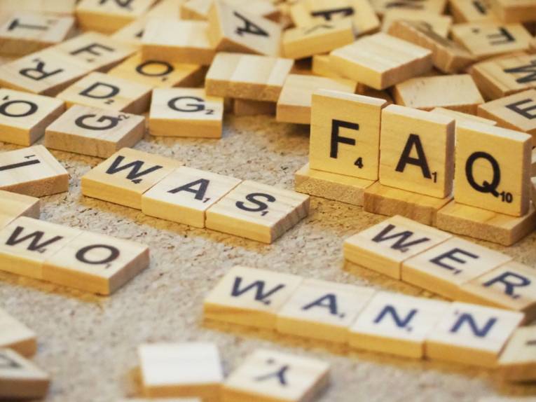 Holzbuchstaben liegen durcheinander, erkennbar sind Frageworte und auf hochkant stehenden Holzplättchen: "FAQ"