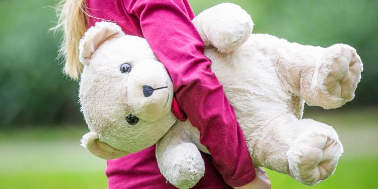 Ein Kind hält einen großen Teddybären unter dem Arm.