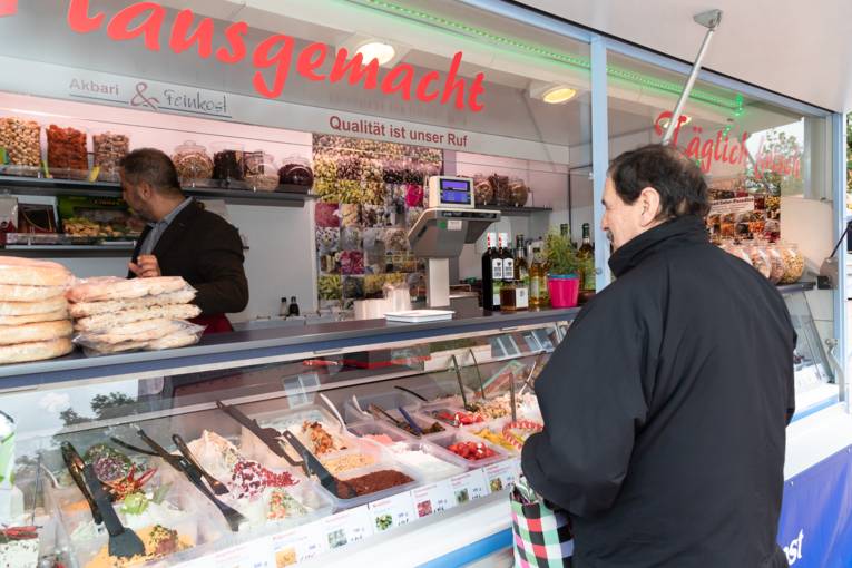 Verkäufer und Kunde an einem Marktwagen, wo Feinkost verkauft wird.