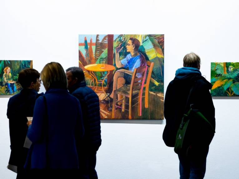 Publikum blickt auf Werke im Regionshaus, Schauplatz für Kunst. Die Bilder zeigen Menschen in farbenfroher tropischer Natur.