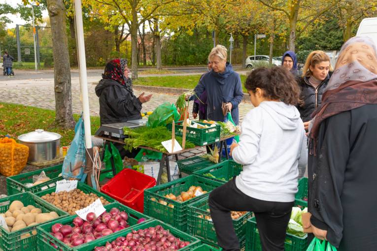 Verk&auml;uferin und Kundschaft an einem Gem&uuml;sestand.