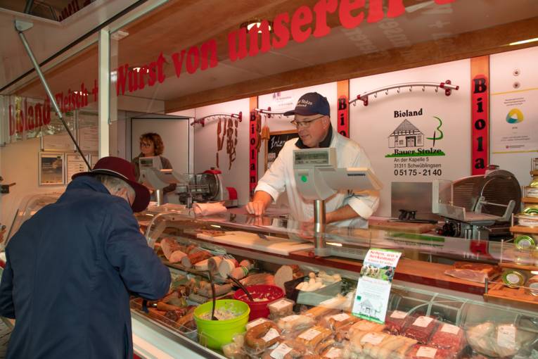 Ein Kunde kauft frische Wurstwaren auf einem Marktstand.