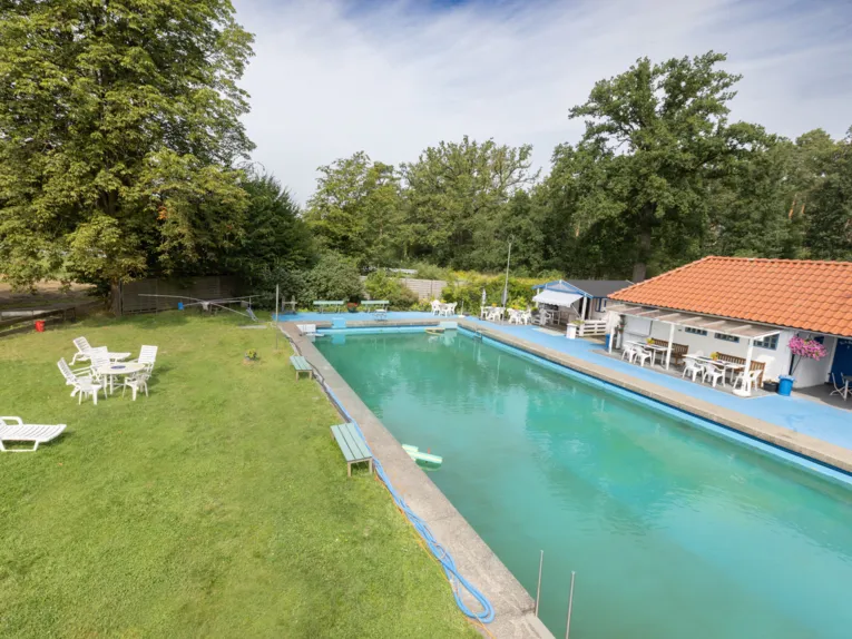 Schwimmbecken, im Hintergrund ein Geb&auml;ude und diverse Sitzm&ouml;glichkeiten sowohl vor dem Geb&auml;ude als auch auf der Wiese