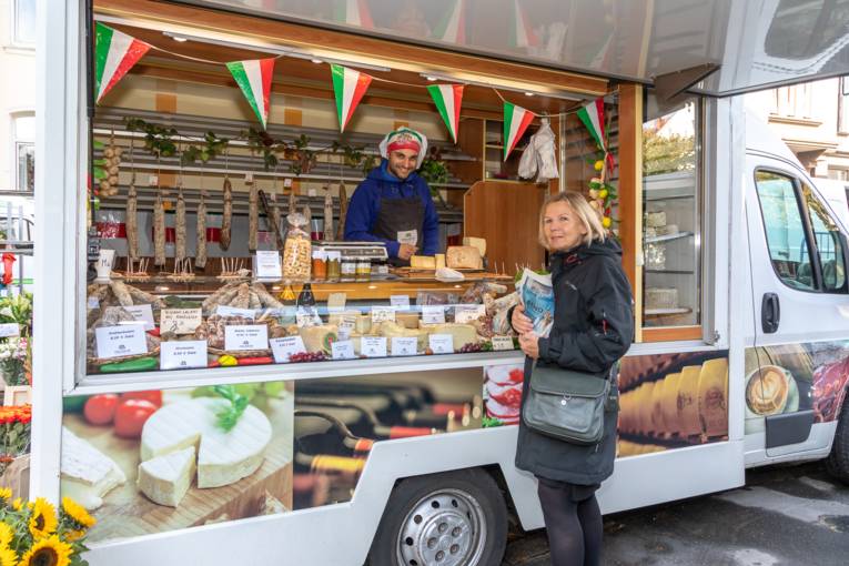 Ein Verkäufer bietet einer Kundin italienische Wurst- und Käsewaren an.