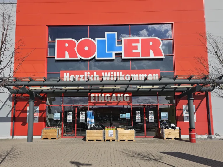 Vista exterior de la tienda de muebles ROLLER en Garbsen, con una fachada de color rojo anaranjado, un gran logotipo de ROLLER y una zona de entrada acristalada.