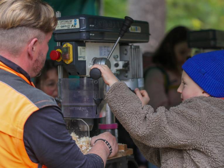 Ein Kind an einer Holzsägemaschine. Daneben steht ein Erwachsener.