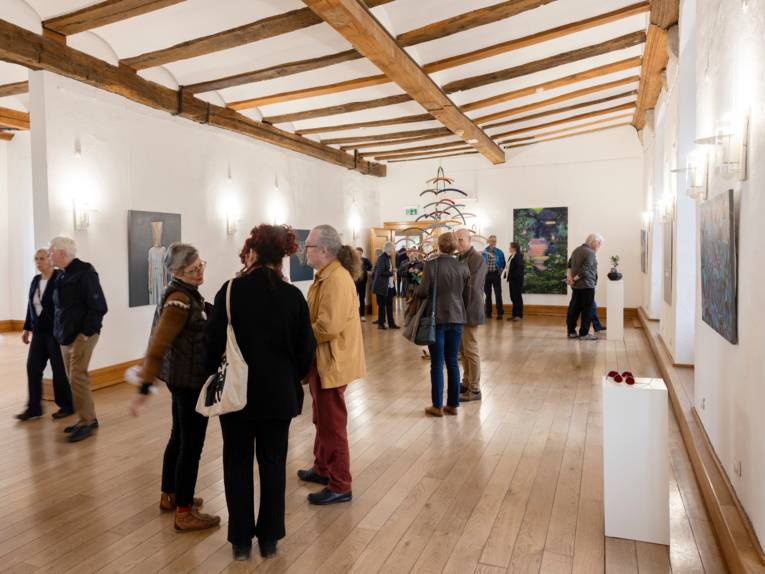 Publikum blickt auf Werke im Schloss Landestrost oder führt Gespräche untereinander.