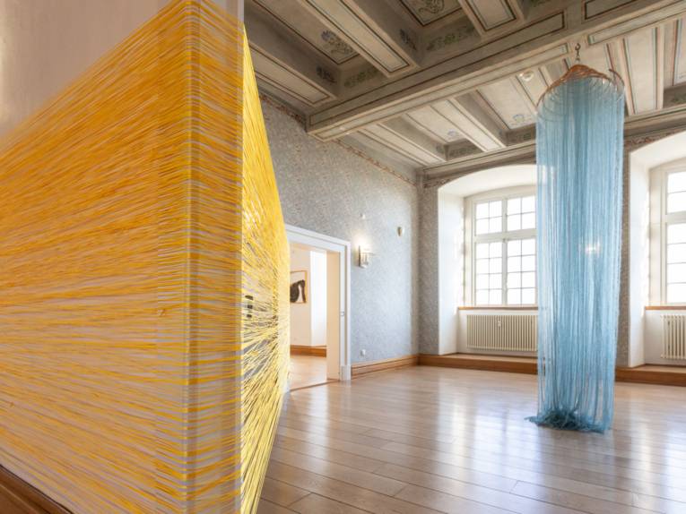Mit gelben und blauen Fäden verkleidete Objekte in einem Raum