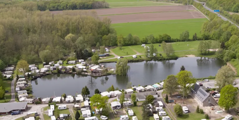 Luftaufnahme eines Natursees mit Gebäuden, Wohnwagen und Wald