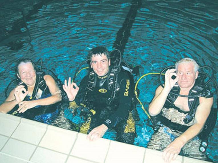 Drei Taucher im Hallenbad, die das OKAY-Zeichen geben