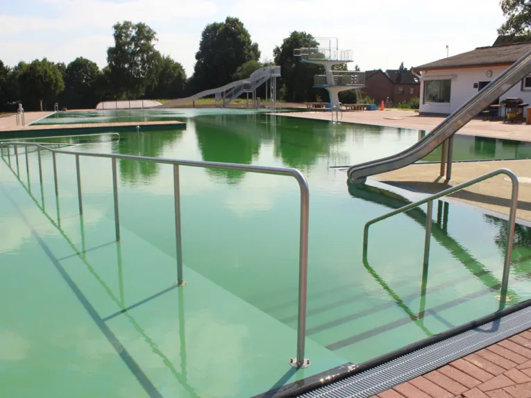Einstieg ins Schwimmbecken über Stufen und mit Handläufen, rechts und im Hintergrund je eine Rutsche