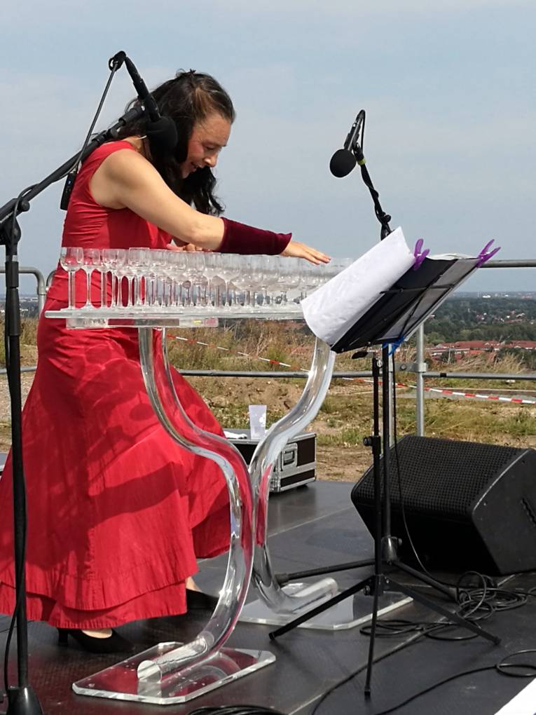 Eine Frau gibt ein Glasharfenkonzert und bringt verschiedene Trinkgläser mit unterschiedlichen Füllständen zum Schwingen.