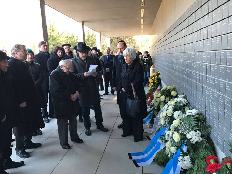 Viele Personen bei einer Kranzniederlegung vor einer Gedenkwand.