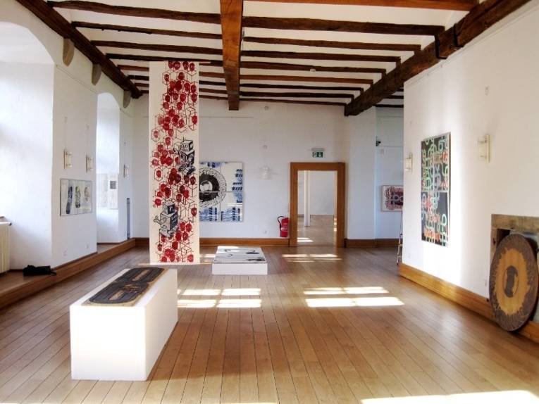Kunst von Harald Schiel ist in einem Saal von Schloss Landestrost ausgestellt. Unter der Decke sind Holzbalken, die Wände sind weiß und der Fußboden besteht aus Parkett.