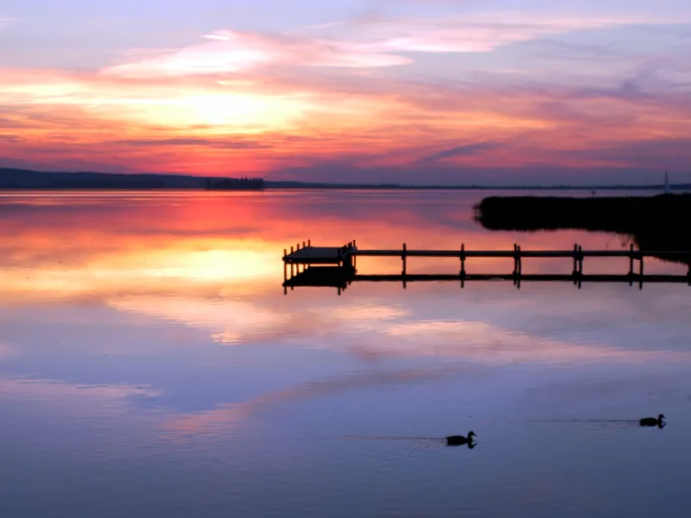 Ein Steg ragt dunkel ins Steinhuder Meer. Der Himmel leuchtet im Sonnenuntergang in verschiedenen Rottönen.