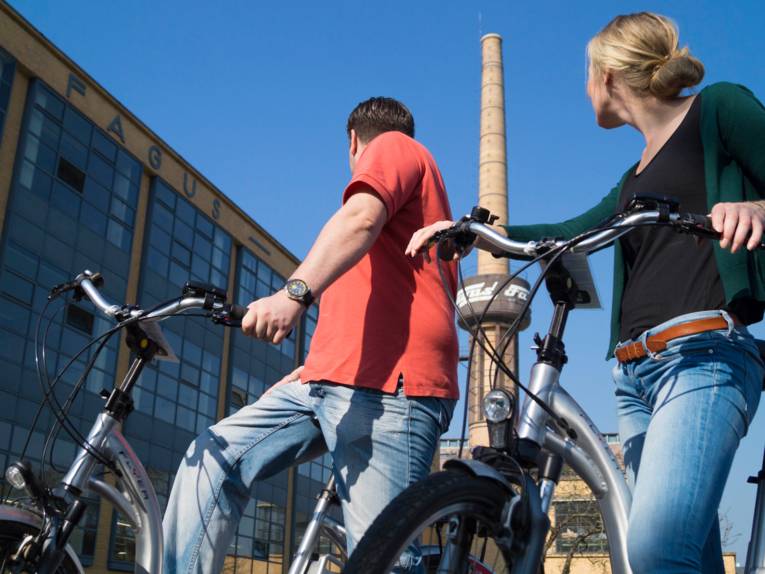 Zwei Radfahrer von einem Industriegebäude mit Schornstein