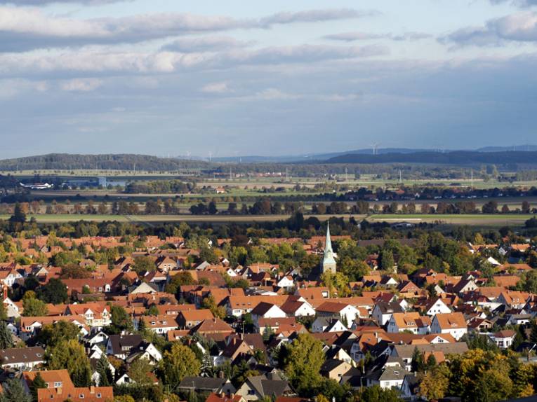Vorne geht der Blick über die Dächer der Stadt Springe, dahinter zeichnet sich eine Landschaft mit Wald, Wiesen, Windrädern und Erhebungen des Deisters ab.