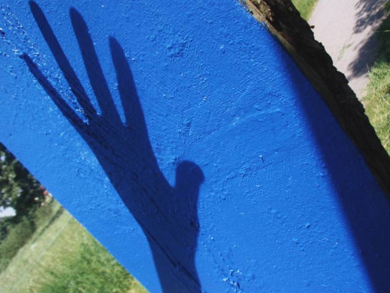 Schatten einer Hand auf einem leuchtend blauen Betonpfahl