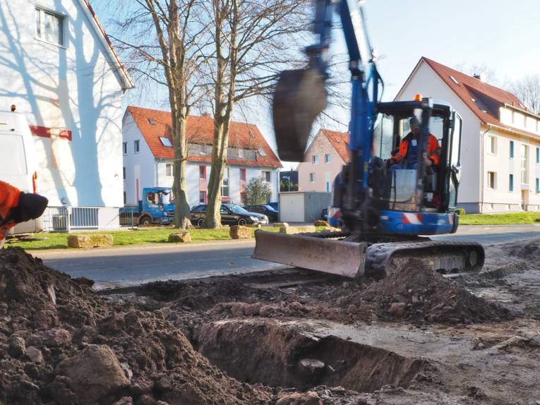 Zwei Bauarbeiter arbeiten mit einem Bagger an einer Straße.